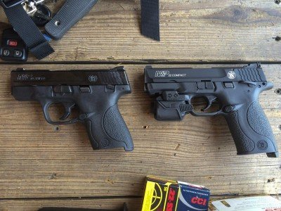 The new M&P22 Compact is shown here (right) next to a Smith & Wesson Shield (left). I put a Crimson Trace Rail Master laser on my test gun because... Fun!