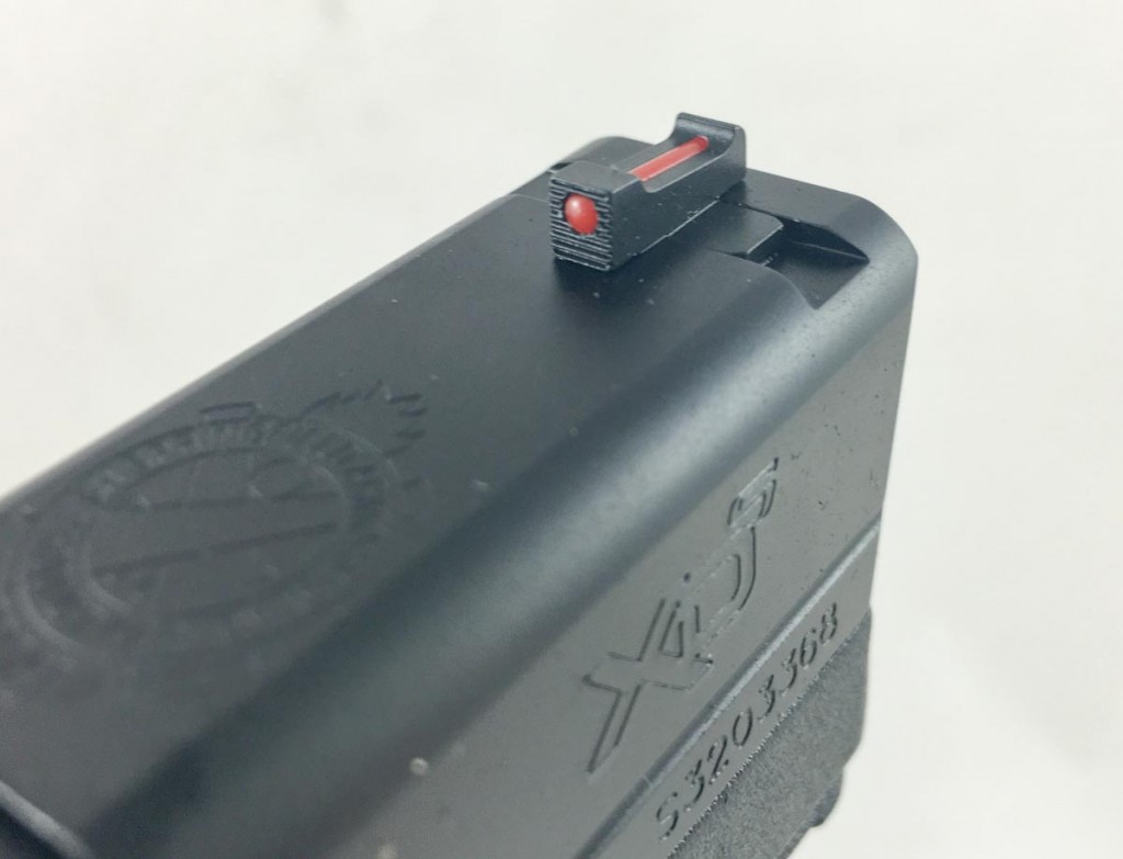 The front sight is a fiber optic tube. The rear sight is a notch flanked by two white dots. 