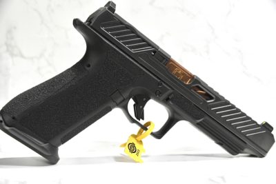 A black, Glock-like handgun, standing on it's brass colored muzzle with a white background.