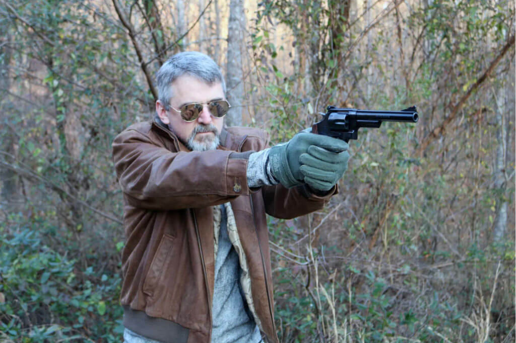 Man in leather jacket shooting the S&W Model 29.44 Magnum handgun in the woods