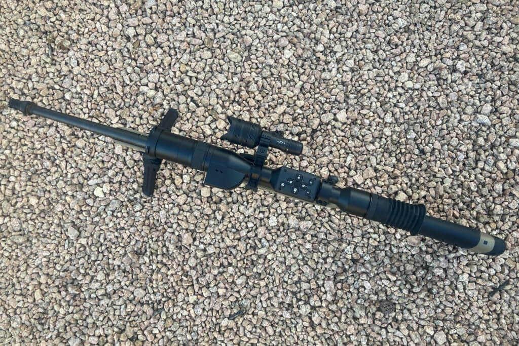 ATN X-Sight 5 LRF mounted on rifle laid 
on gravelly ground