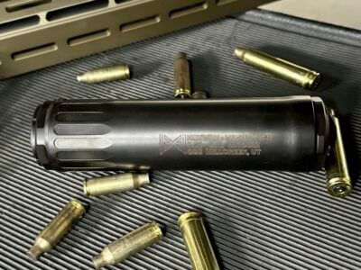 A black suppressor sits among rifle brass on a table.