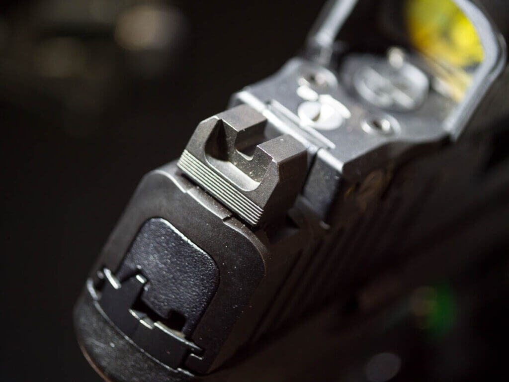 Close up of the rear sights which are blacked out and serrated. There is a red dot  on top of the slide.