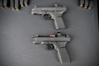 Two handguns are displayed on a black background with loaded magazines peeking out from the top of the picture.