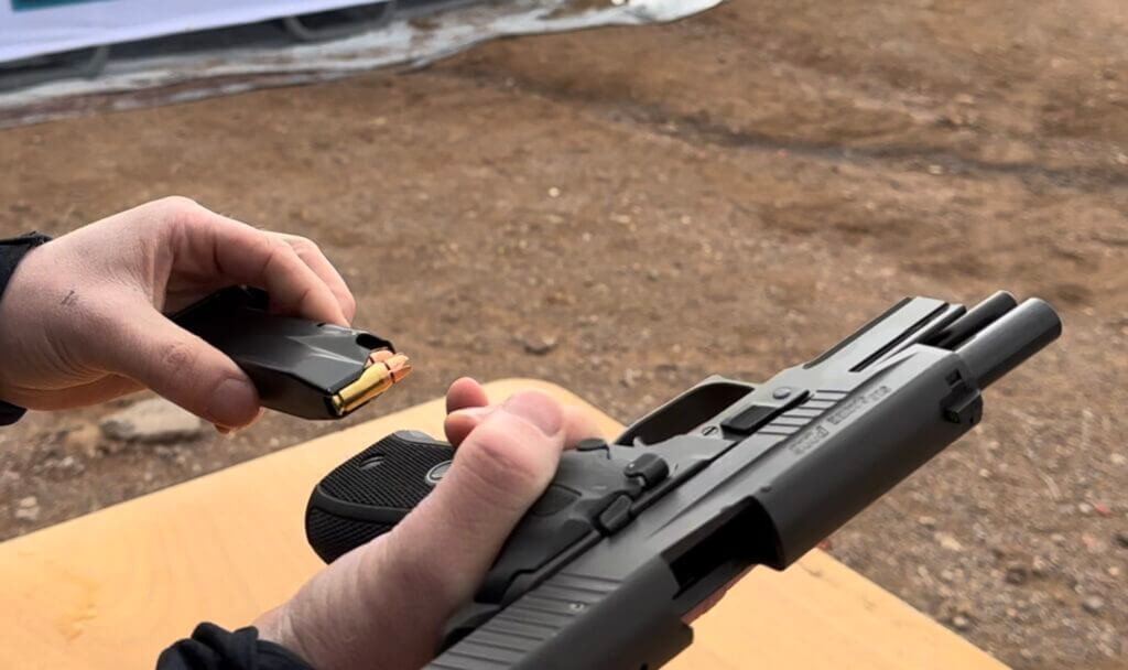 A black handgun is being loaded with a magazine at the gun range.