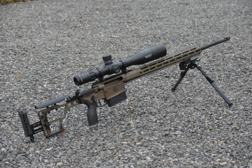 A  tan rifle with a large optic is posed in the gravel.
