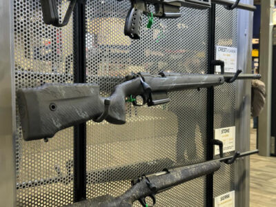 A grey, bolt-action rifle is displayed on the wall.