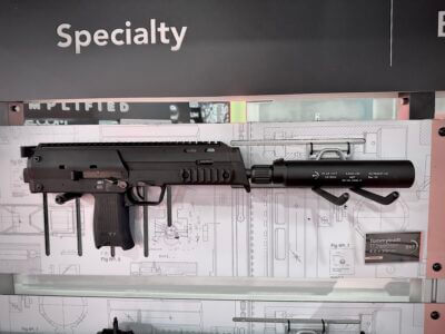 An MP7 clone is displayed on a wall with a background of engineering blueprint designs.