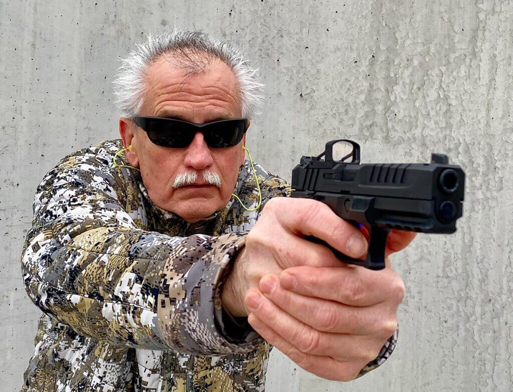 Man aiming pistol with the RMSc red dot in front of cement wall