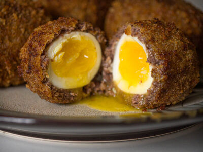 Close up of Scotch eggs, one cut open on a plate.