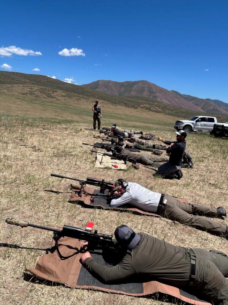 Shooters lying prone on grassy hill sighting in scopes on rifles
