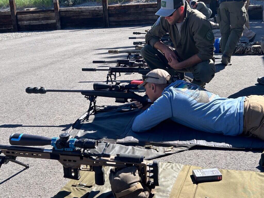 Man lying prone on asphalt looking through a Leupold Mark 4HD scope mounted to a rifle