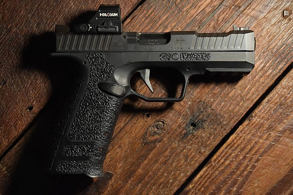 A black handgun lays on a wooden table top.