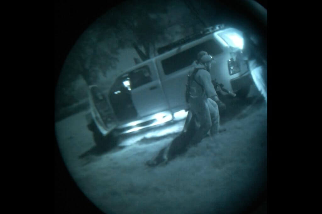 screen shot of man dragging hog through blue-green night vision