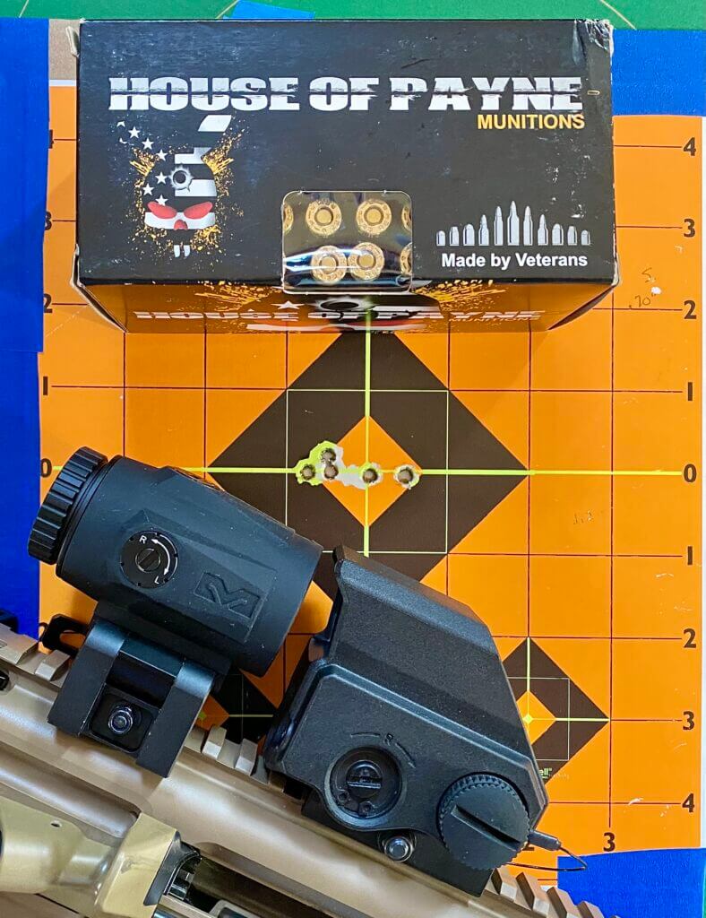 Orange target with 5 bullet holes with ammo box and Meproguard MMX3 Magnifier