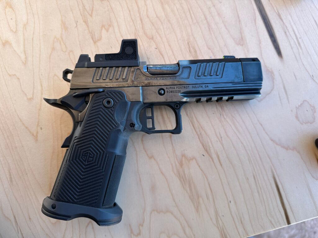 A highly polished black handgun sits on a wooden table, pointing to the right. 