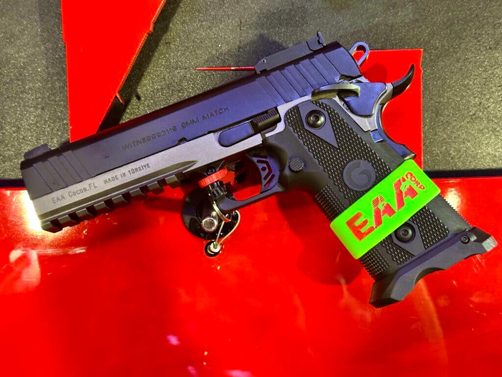 A black handgun lays on a red background. It is laying on it's side and pointing to the left.