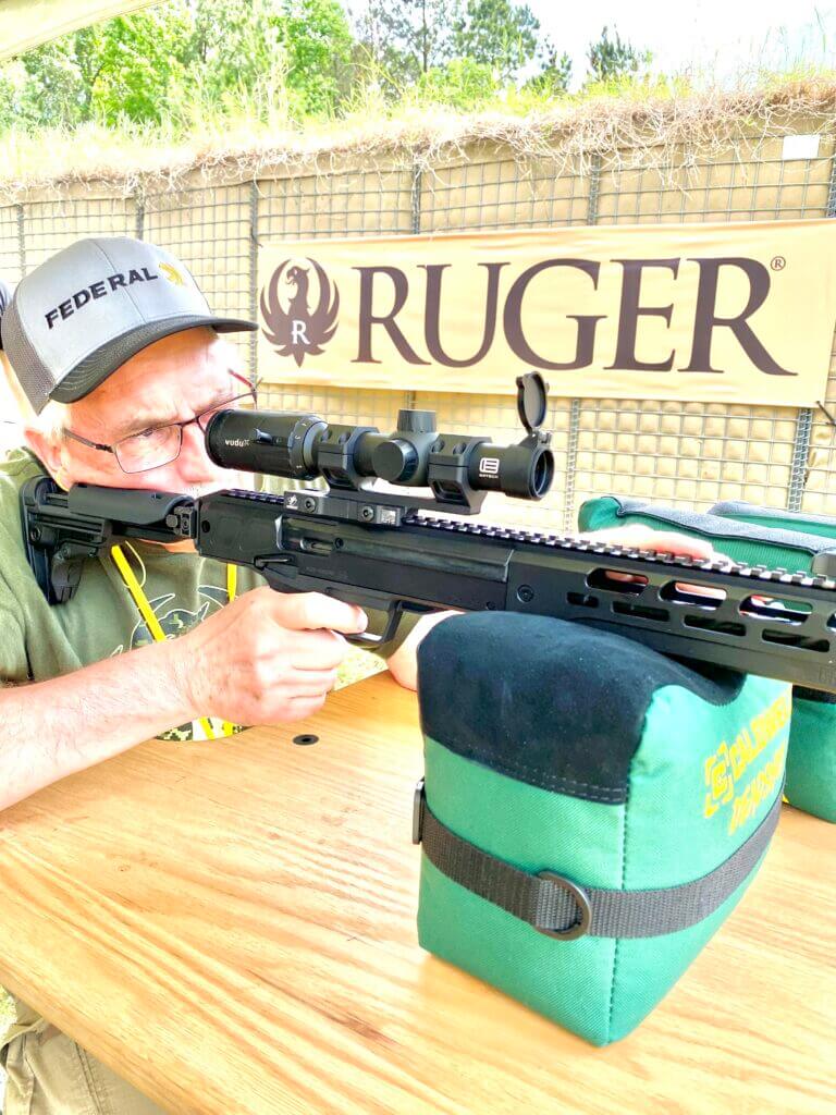 Man shooting rifle with green range bag